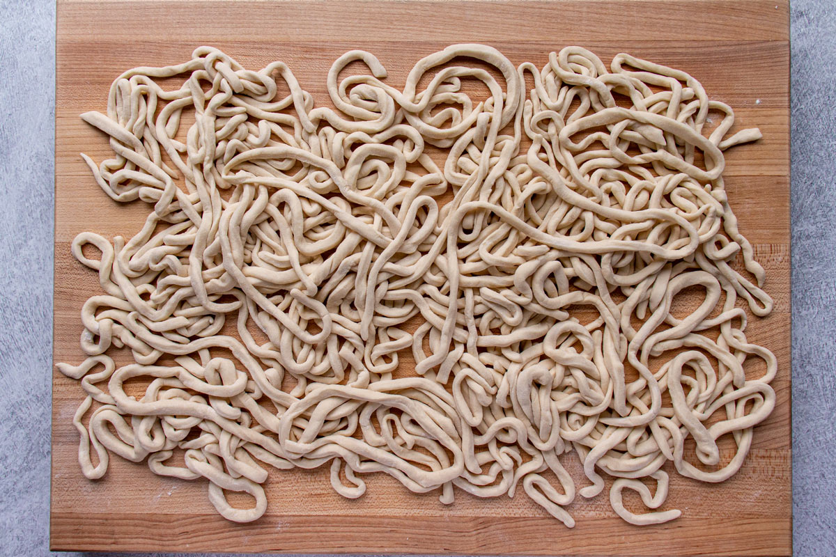 Homemade udon noodles tossed with flour on a wooden cutting board.