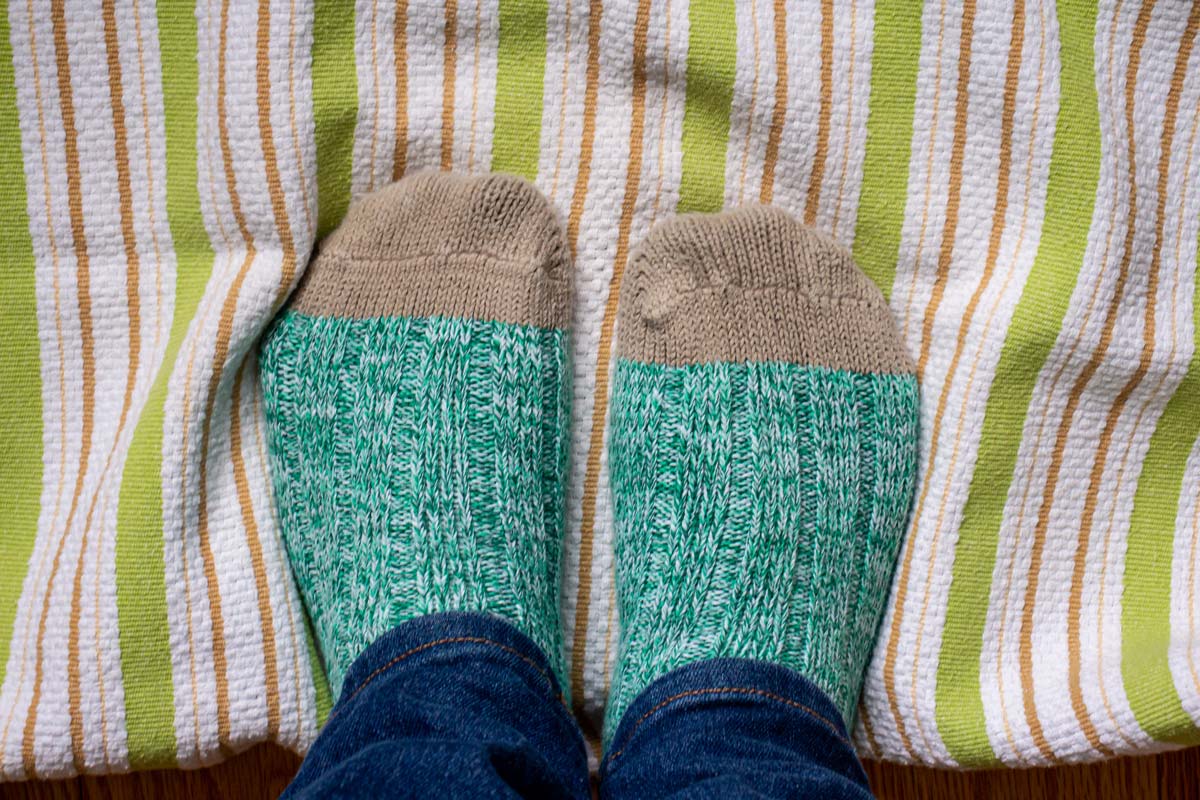 Two feet in green socks with tan toes standing on a striped towel.