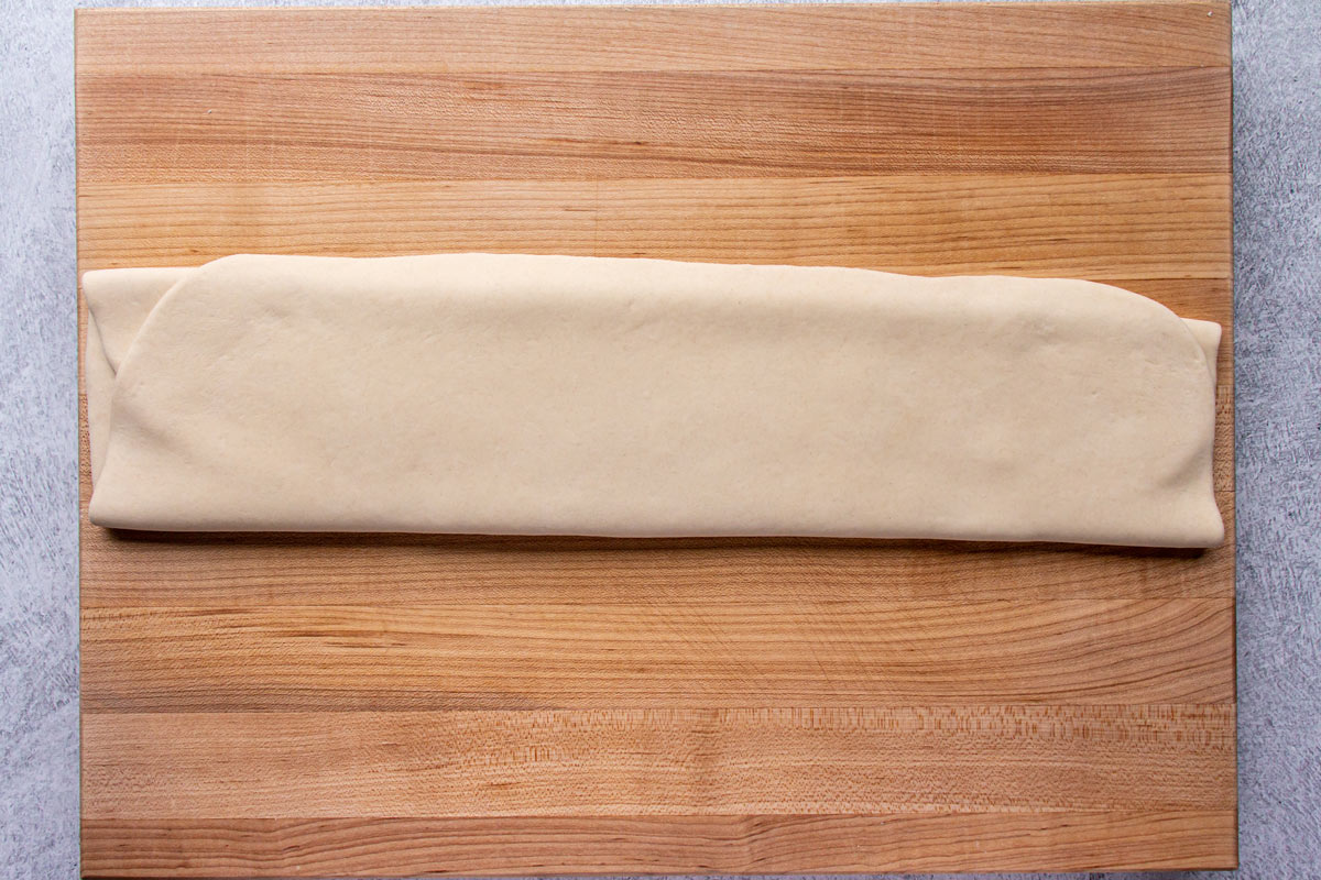 Dough folded into thirds to create a long strip on a wooden board.