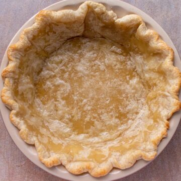 A partially baked pie crust on a beige background.