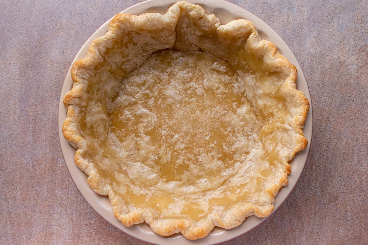 A partially baked pie crust on a beige background.
