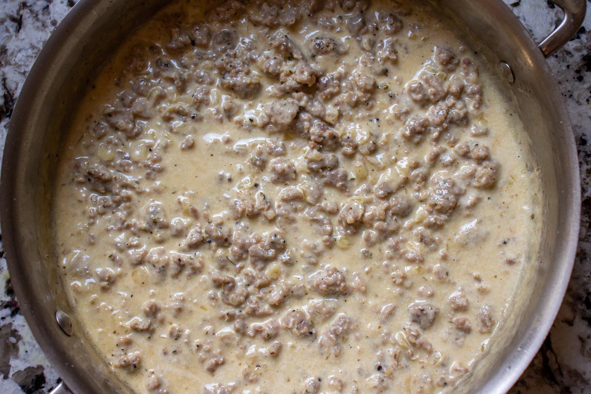 A creamy sauce with cooked crumbled pork sausage in a stainless steel sauté pan.