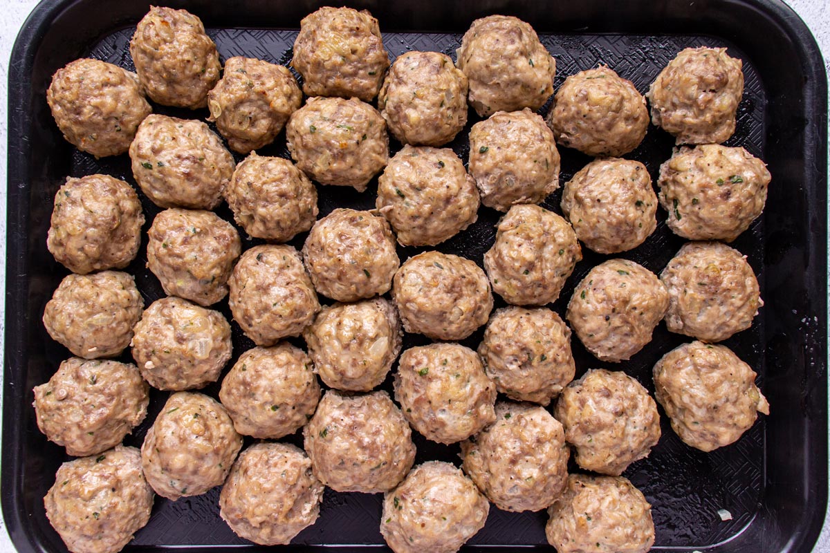 Meatballs arranged in a single layer on a black plastic cafeteria tray.
