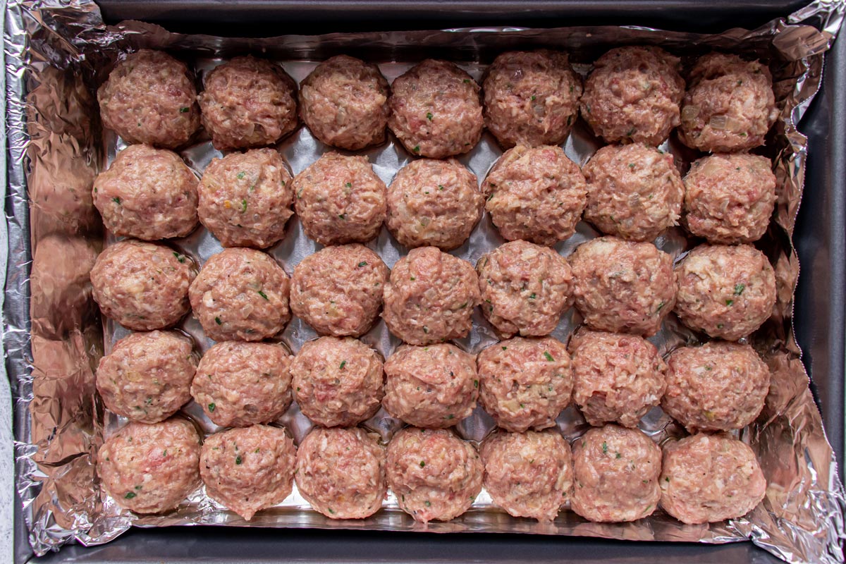Uncooked meatballs tightly arranged into a grid pattern in a rectangular baking pan.