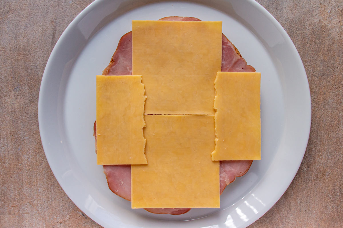 Sliced ham and cheese on top of bread slices on a white plate.