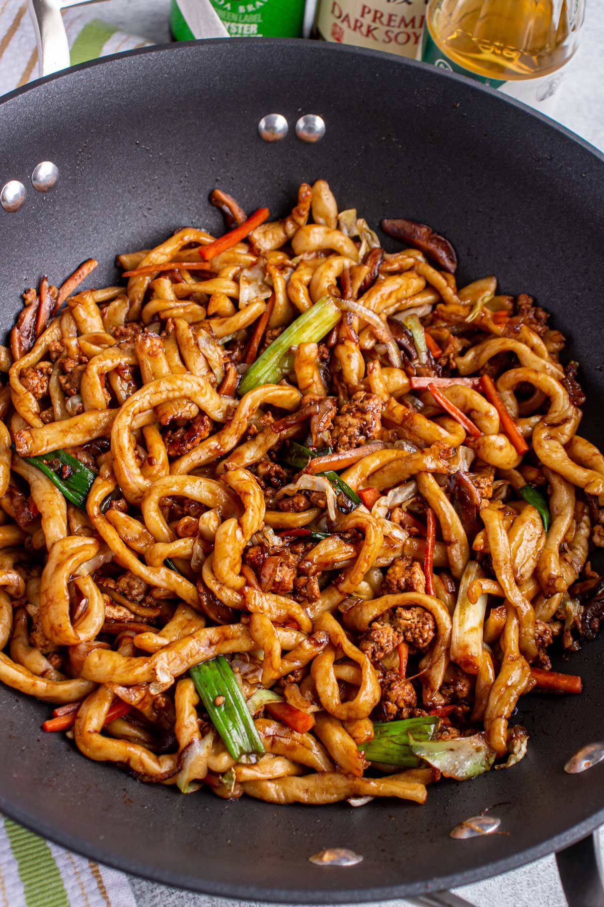 Stir-fried yaki udon noodles with scallions, carrots, cabbage, and ground pork in a wok.