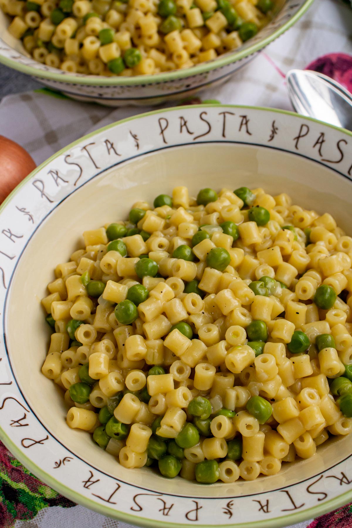 A bowl that says pasta repeatedly around the edges filled with ditalini and peas.