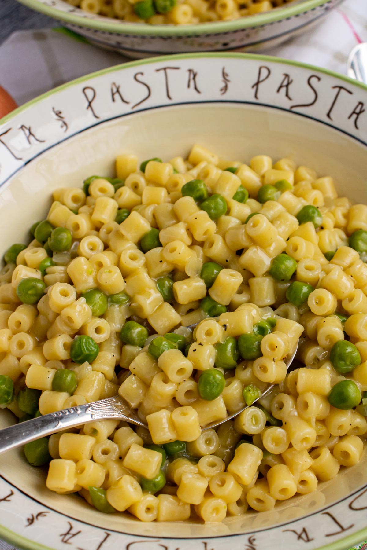 Closeup of a spoon lifting ditalini pasta and peas out of a bowl.