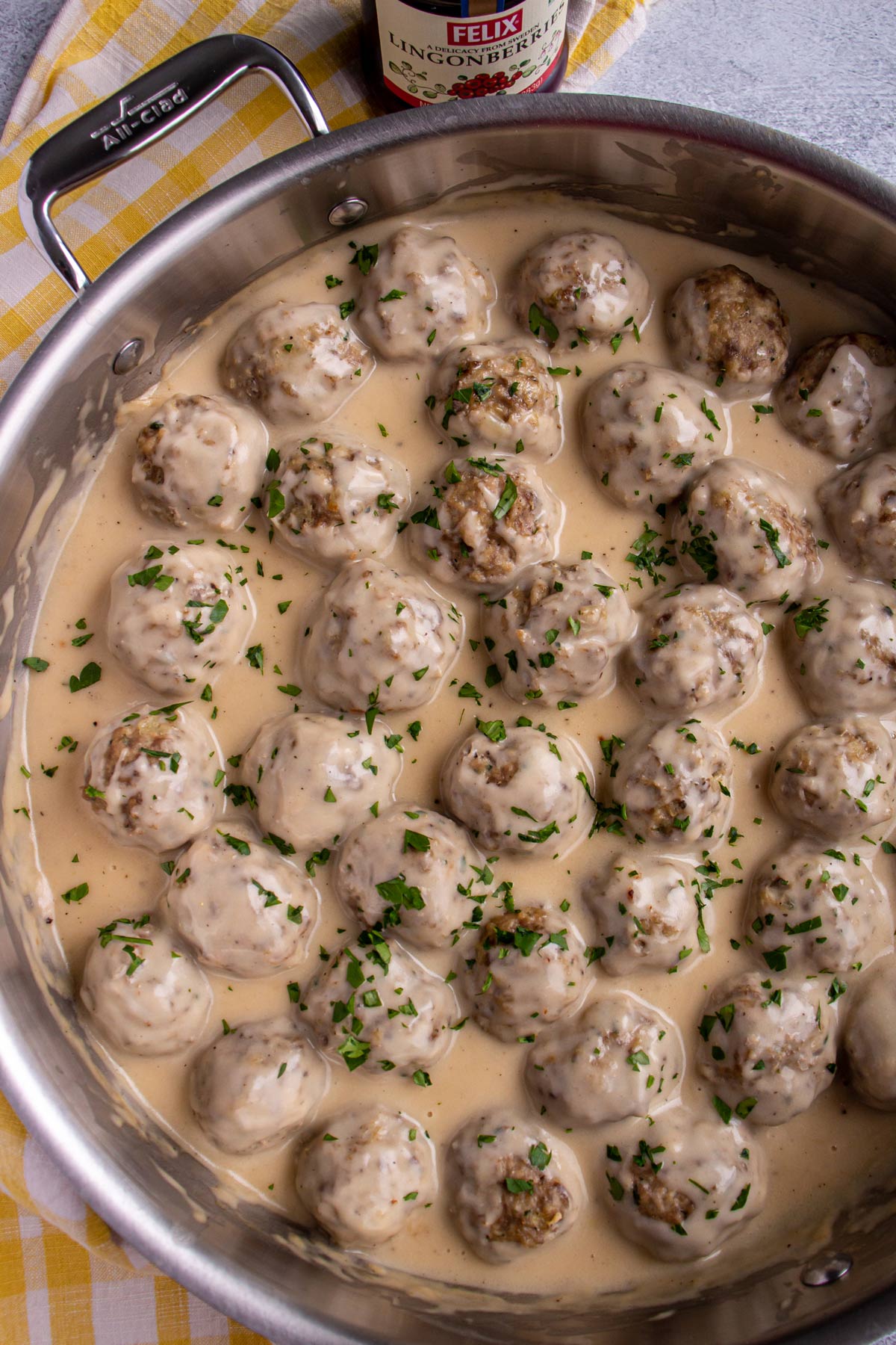 Swedish meatballs in creamy gravy topped with chopped parsley in a stainless steel skillet.