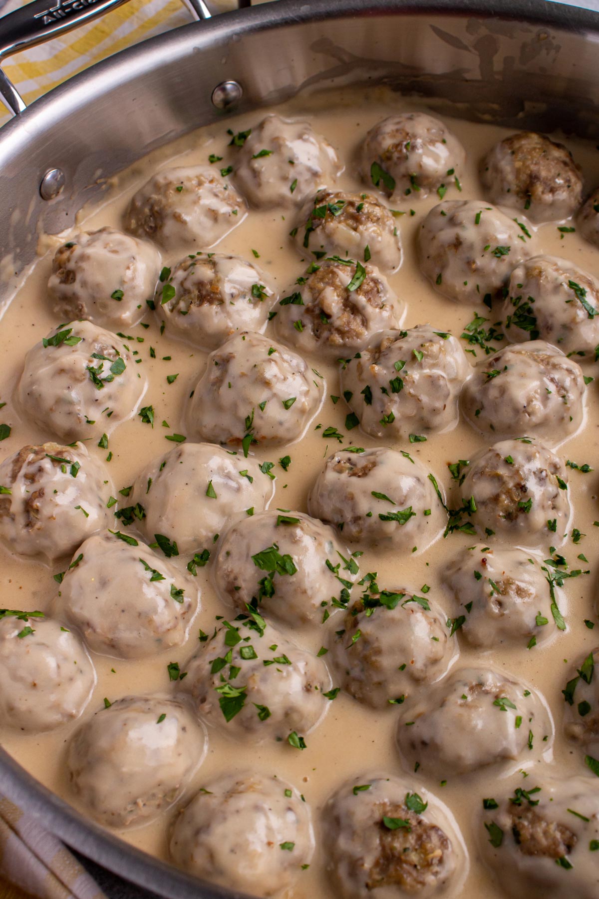 Swedish meatballs with creamy gravy and topped with chopped parsley in a wide metal skillet.