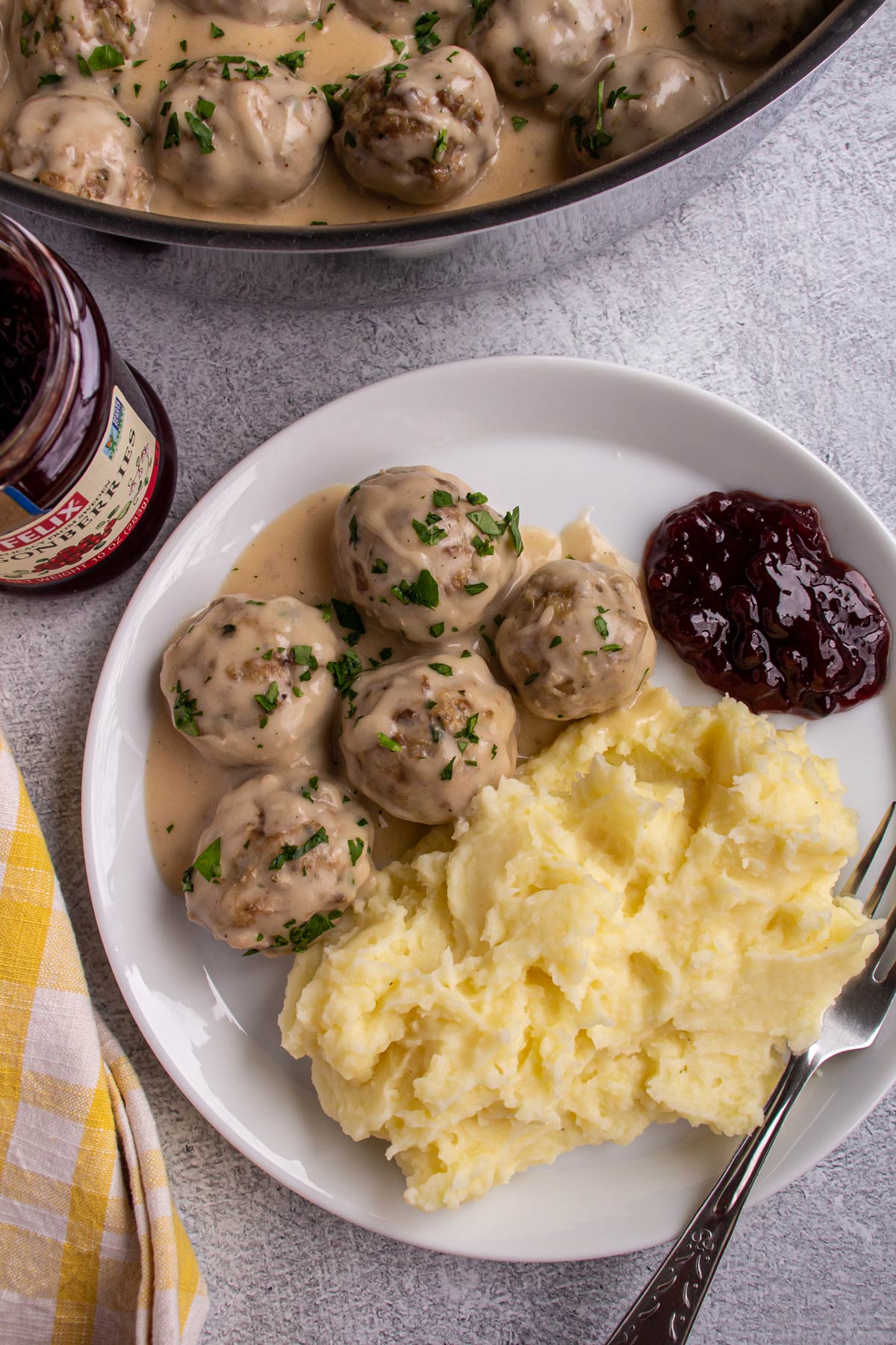 Five Swedish meatballs in gravy served with mashed potatoes and lingonberry preserves on a white plate.