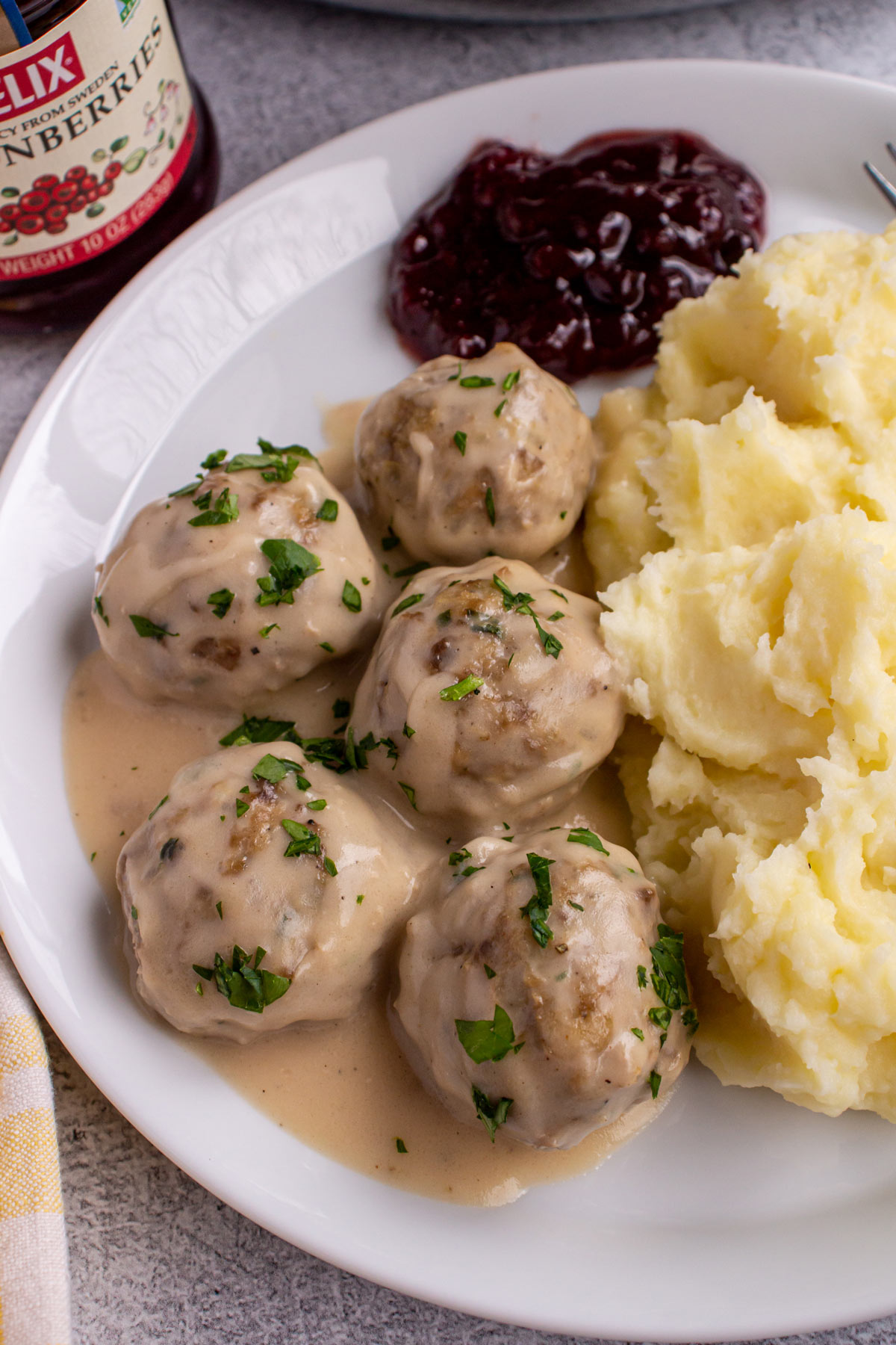 Five Swedish meatballs in gravy on a white plate with mashed potatoes and lingonberry preserves.