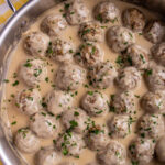 Swedish meatballs in creamy gravy topped with chopped parsley in a stainless steel skillet.