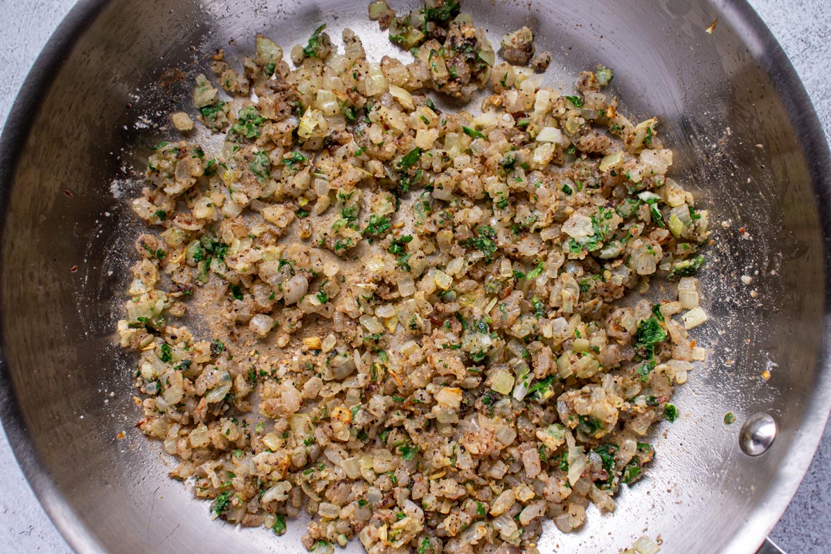 A mixture of sautéed onions, parsley, and spices in a metal skillet.