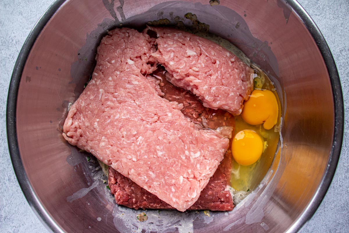 Ground pork, ground beef, and raw eggs in a metal mixing bowl.