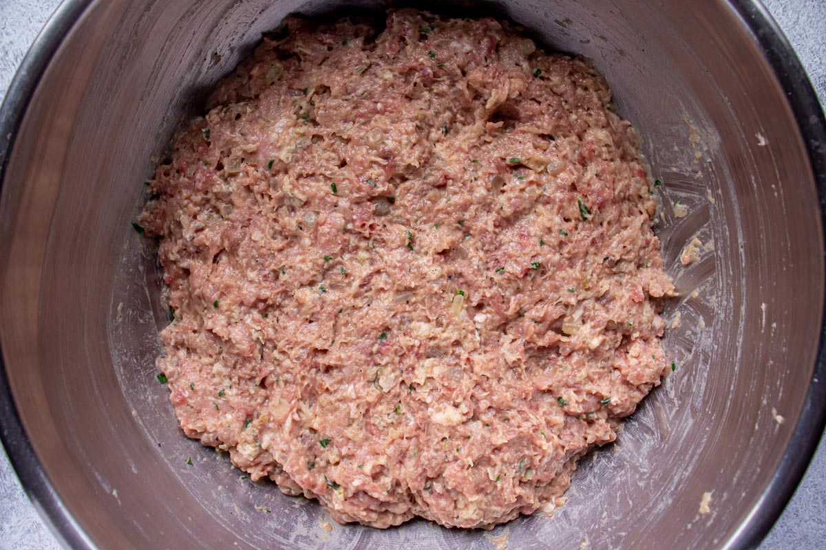 A light pink ground meat mixture in a metal mixing bowl.