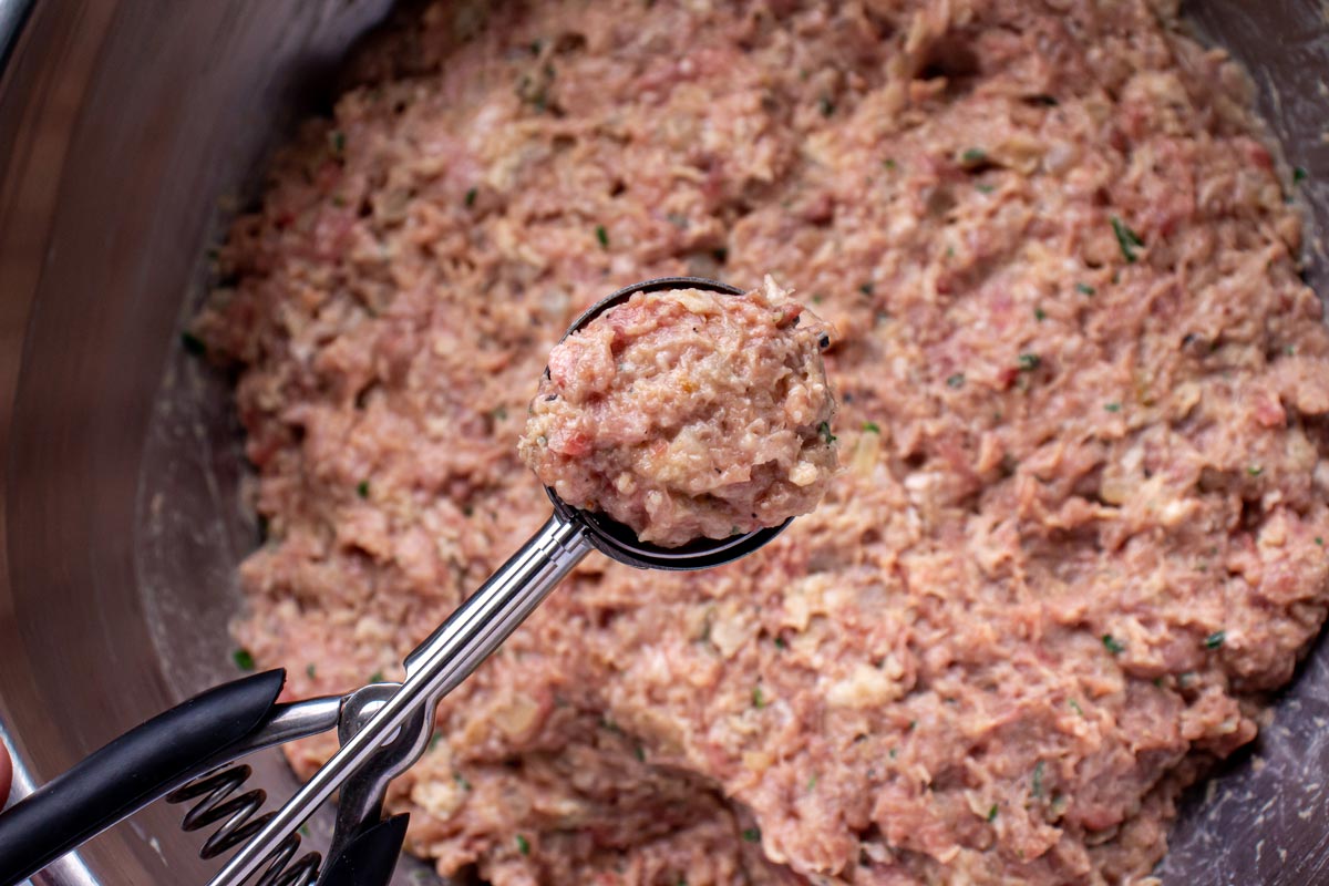 Scooping a ground meat mixture with a cookie scoop to make meatballs.
