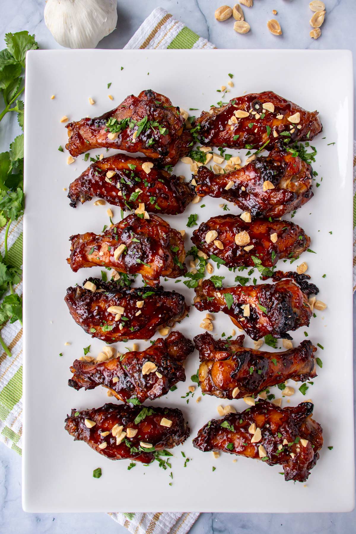 A white rectangular platter of dark brown glazed chicken wings on a striped towel.