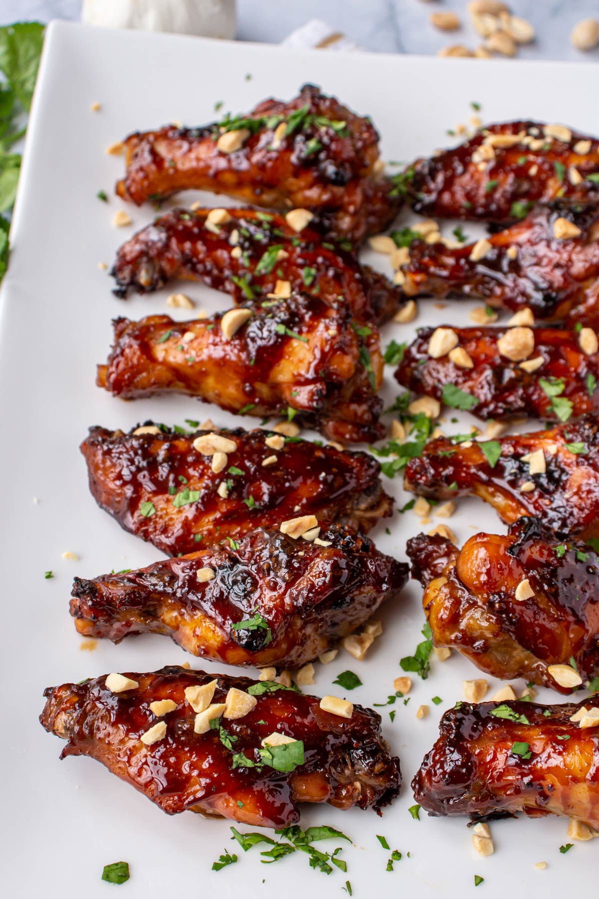 Twelve dark brown glazed chicken wings topped with cilantro and peanuts on a white platter.