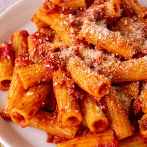 Closeup of rigatoni all' amatriciana topped with grated cheese on a white plate.