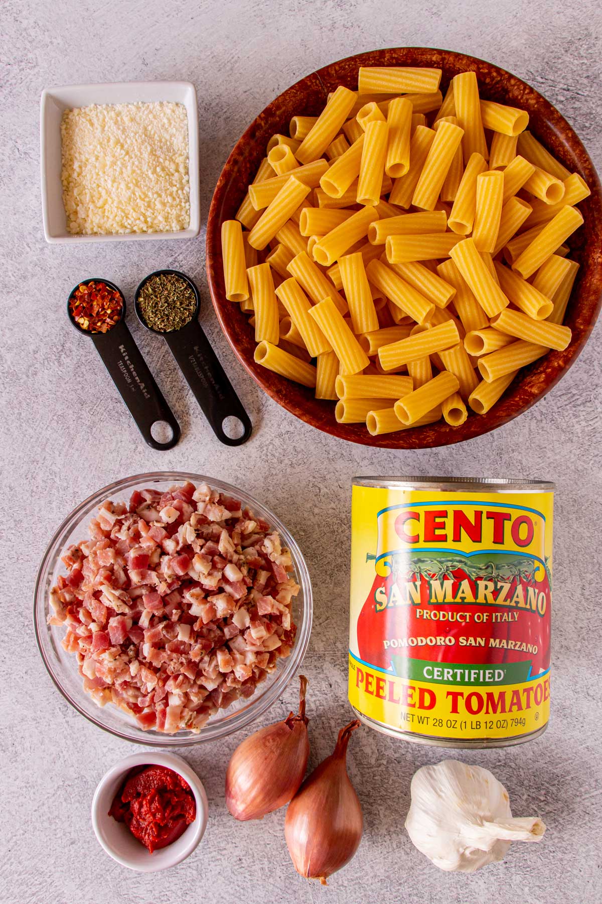 Ingredients for rigatoni amatriciana on a light grey background.