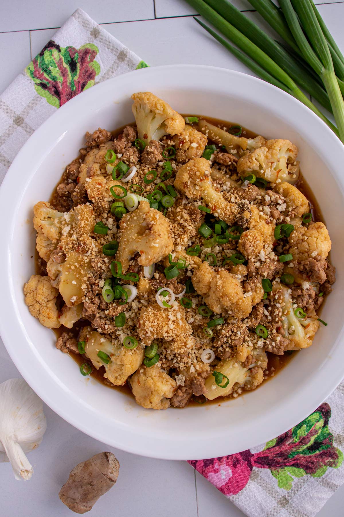 Stir-fried cauliflower with ground pork topped with panko and scallions in a wide white bowl.