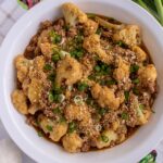 Stir-fried cauliflower with ground pork topped with panko and scallions in a wide white bowl.
