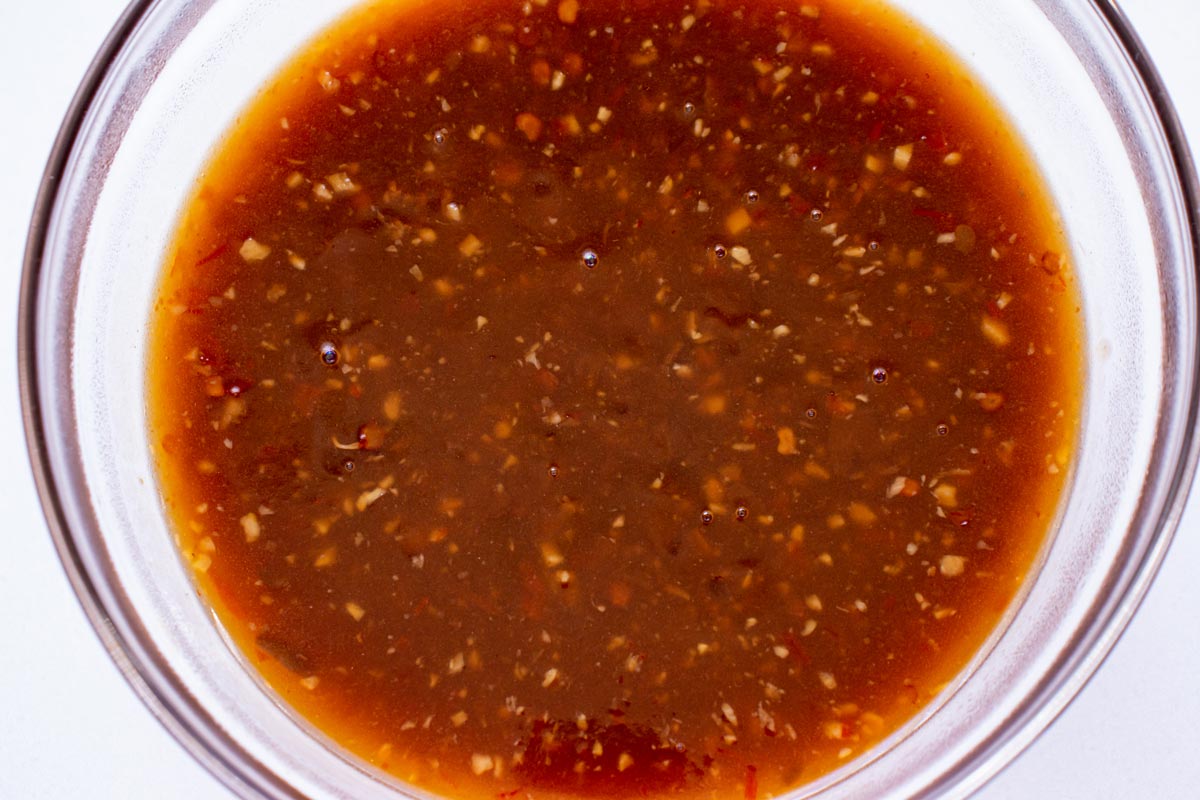 A reddish dark brown sauce with minced garlic and ginger in a glass bowl.