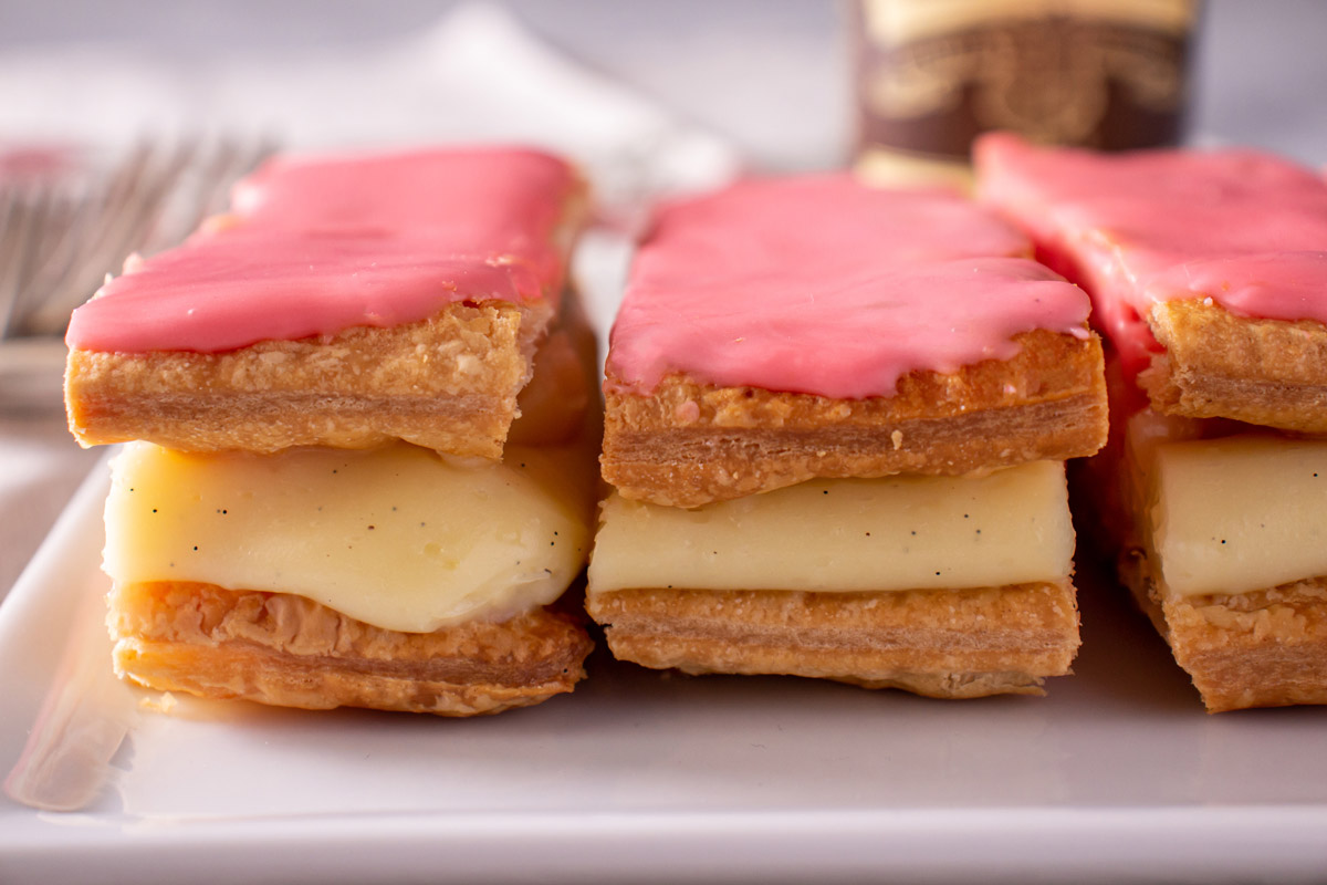 Closeup of puff pastries sandwiched around pastry cream with pink glaze on top.