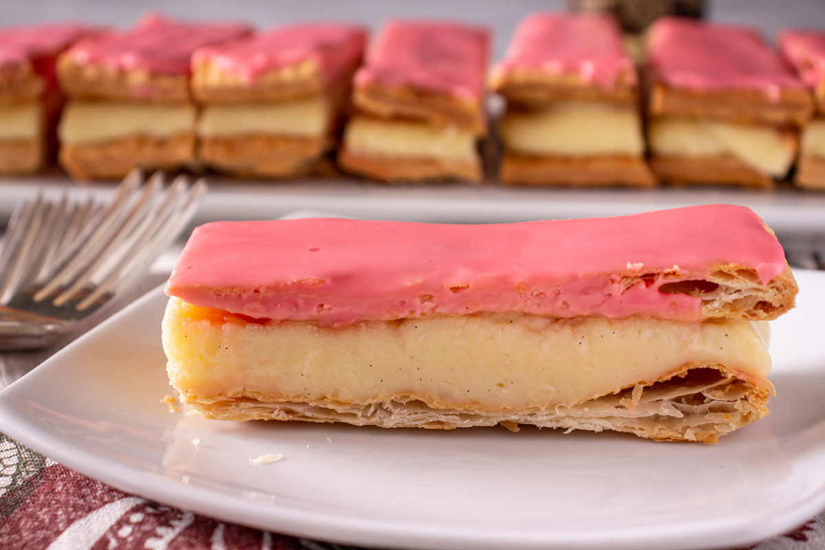 A rectangular tompouce pastry with pastry cream filling and pink glaze on a white plate.