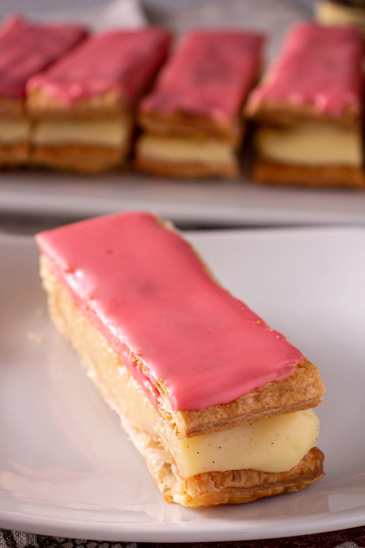 Closeup of a rectangular puff pastry with pastry cream filling and pink glaze on a plate.