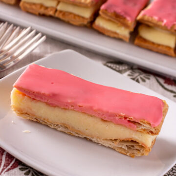 A rectangular Napoleon style Dutch pastry topped with pink glaze on a white plate.