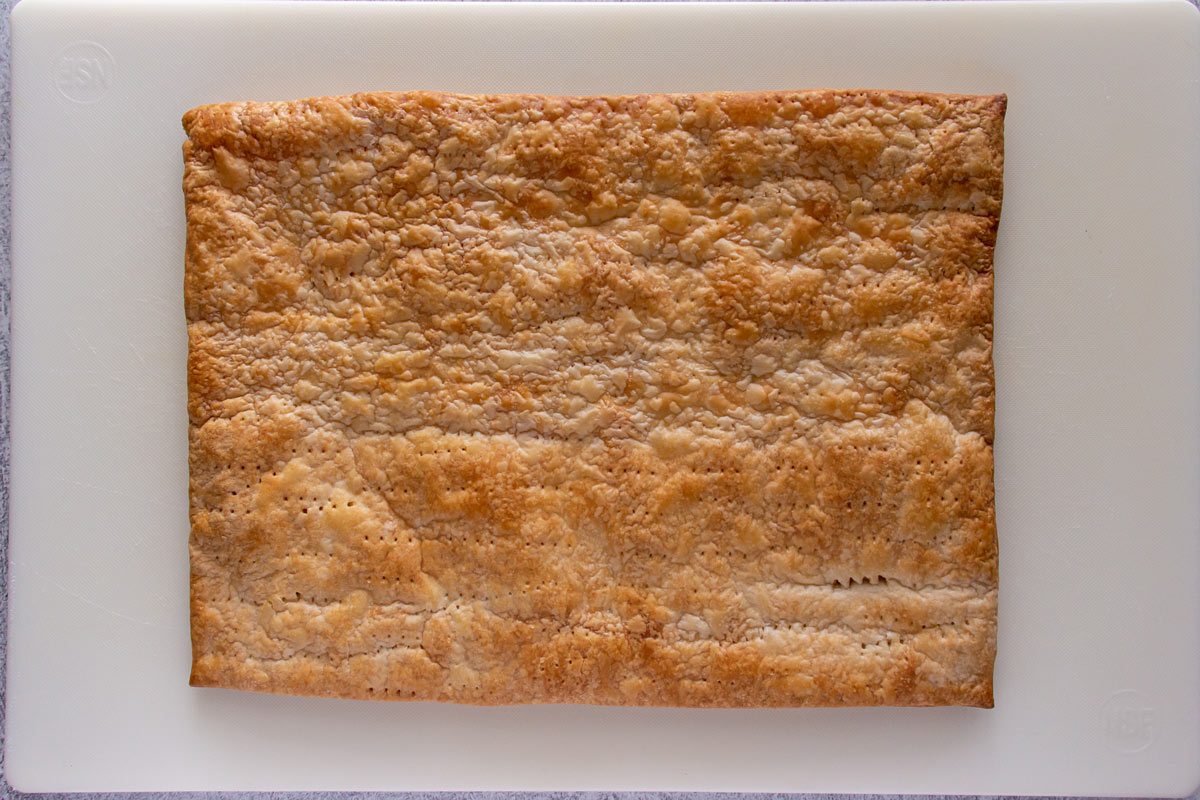 A rectangular sheet of baked puff pastry on a white cutting board.