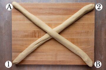 Two long ropes of dough crisscrossed into and X shape on a wooden board.