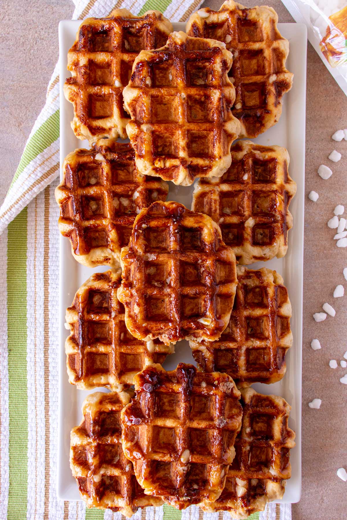 Eleven waffles stacked in rows on a white rectangular platter on top of a striped towel.