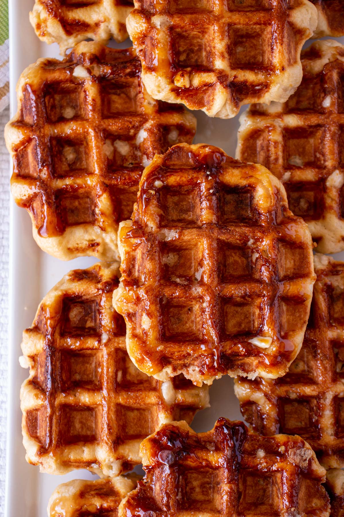 Closeup of shiny caramelized Liege waffles stacked two layers high on a white platter.