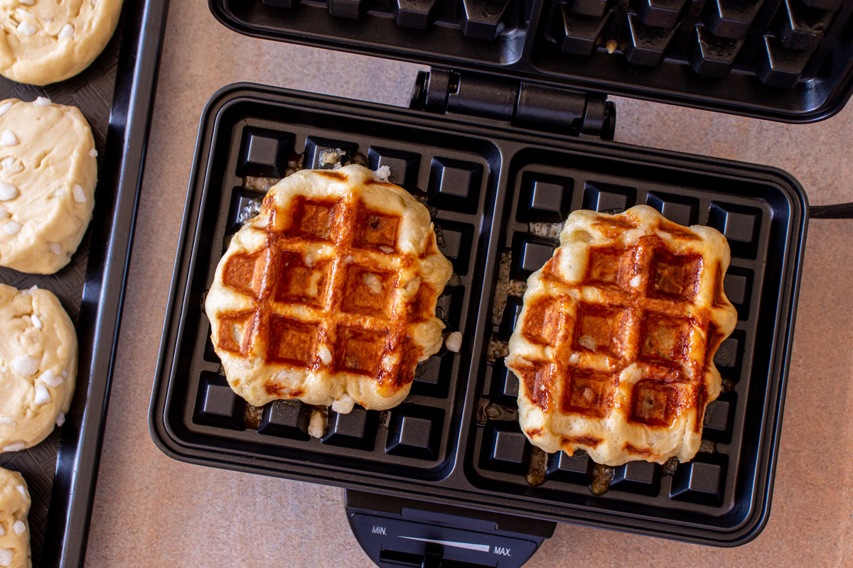 Two cooked pearl sugar waffles in a rectangular waffle iron.