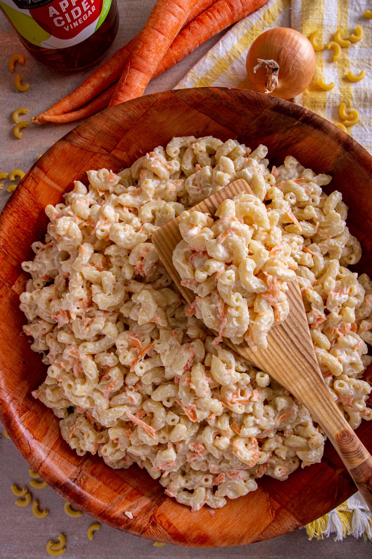Hawaiian macaroni salad in a wooden bowl with a wooden spatula lifting some out.