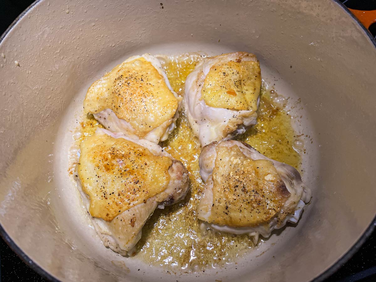 Four skin-on bone-in chicken thighs seared in an enameled Dutch oven.