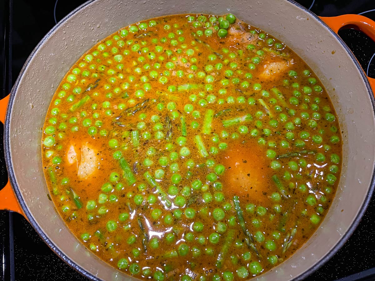 Peas and asparagus pieces in an orange broth with pieces of chicken peeking through the surface.