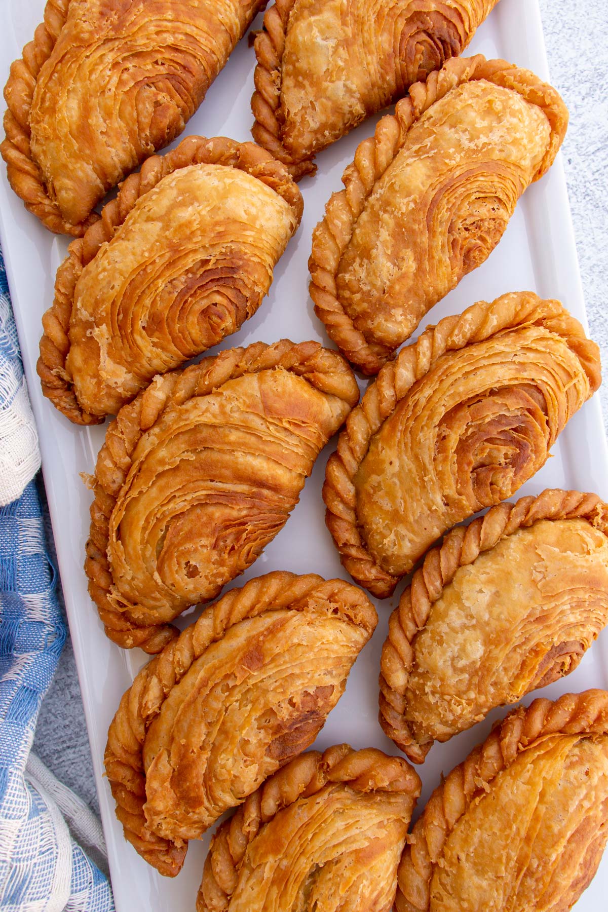 Flaky karipap pusing curry puffs with a spiral pattern in the dough on a white platter.