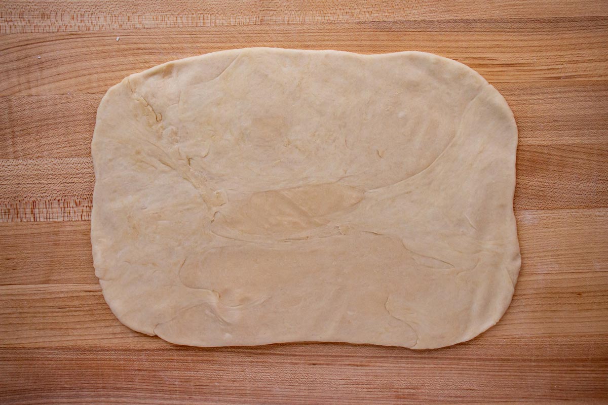 A rough rectangle of rolled out dough on a wooden board.