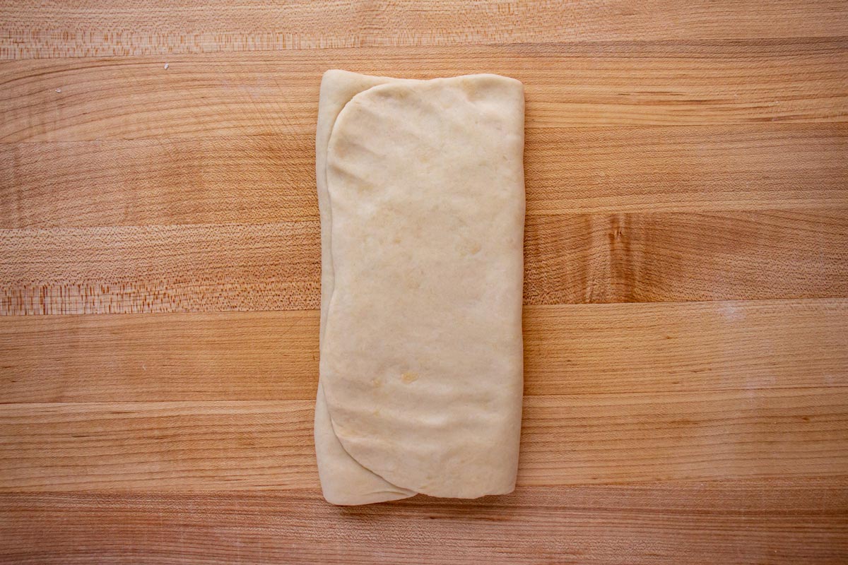 Rolled out dough folded into thirds like a letter on a wooden board.