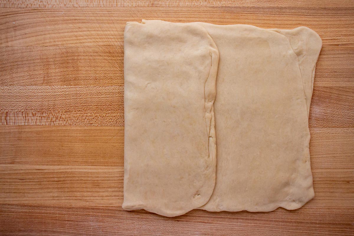 Folding rolled out dough into thirds like a letter on a wooden board.