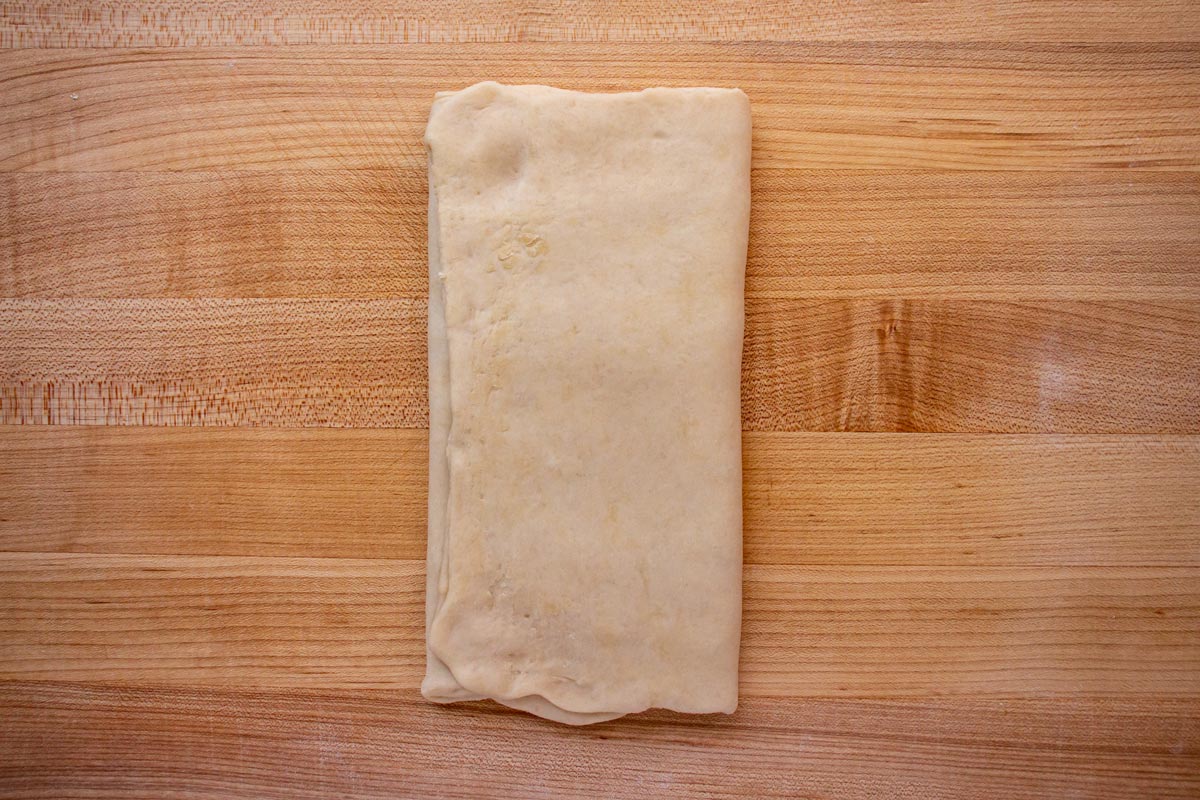 Rolled out dough folded into thirds like a letter on a wooden board.