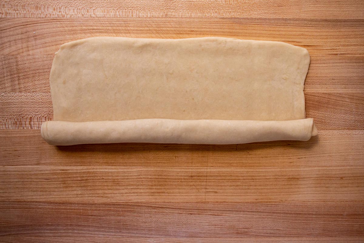Rolling a flat rectangle of dough like a jelly roll on a wooden board.