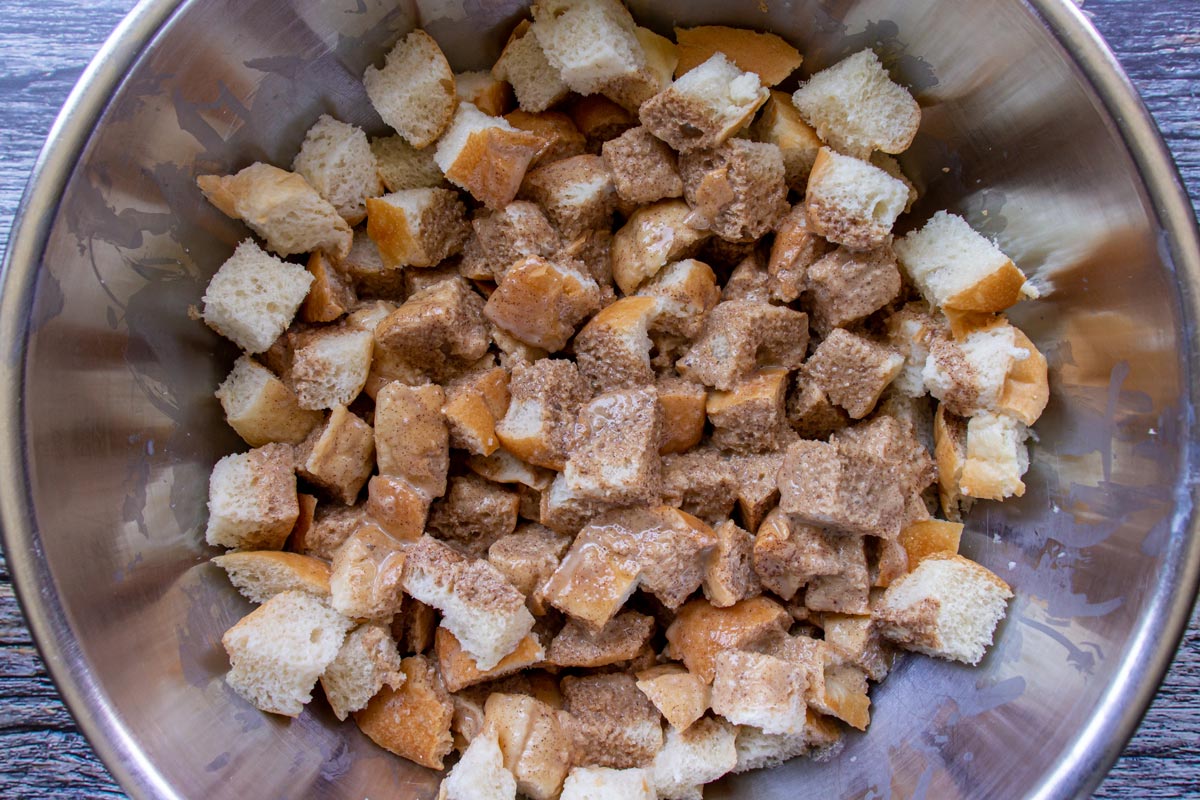 Bread cubes drizzled with a light brown mixture in a metal mixing bowl.