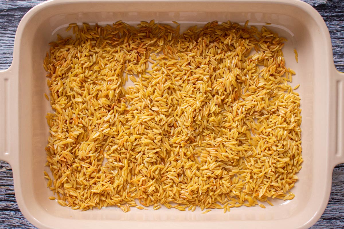 Lightly toasted orzo spread out in the bottom of a rectangular baking dish.