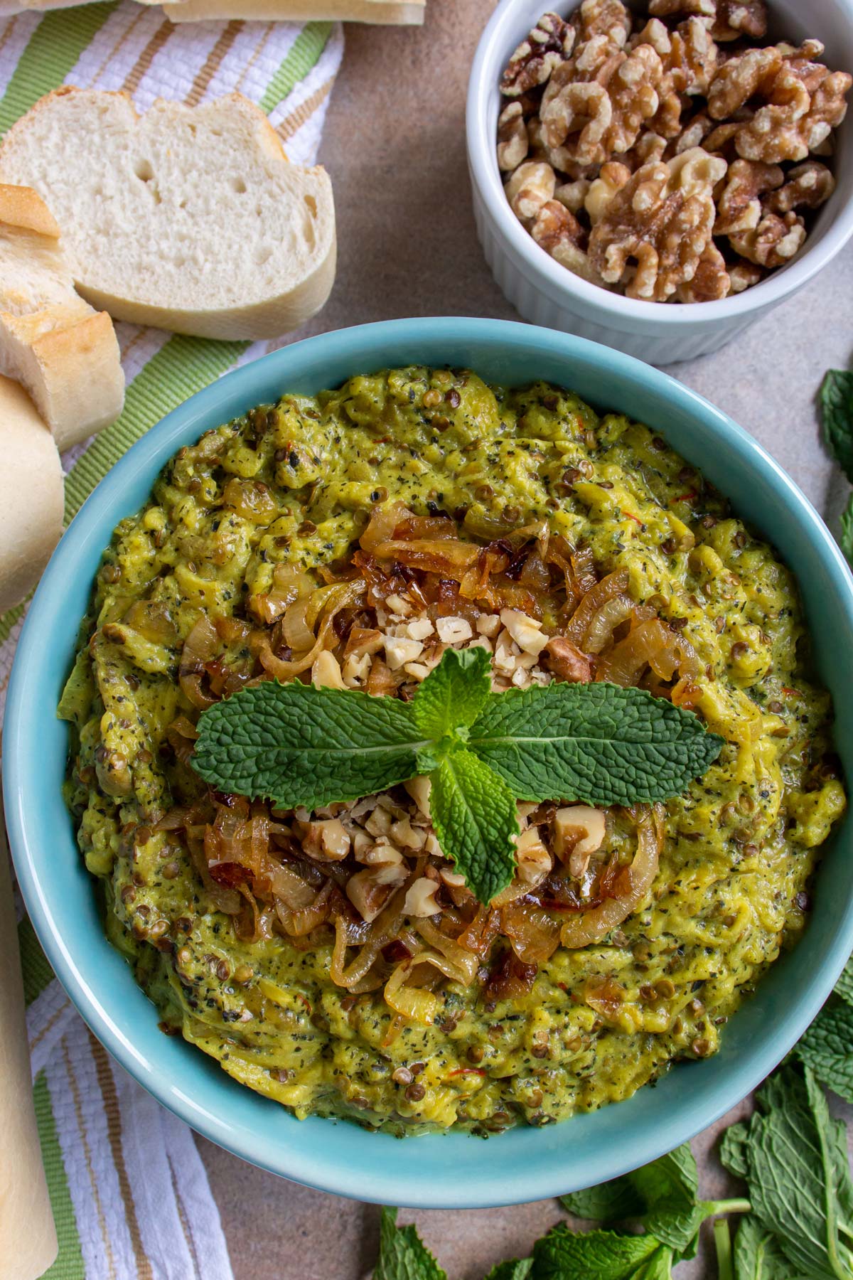 Kashke bademjan eggplant dip in a blue bowl topped with chopped walnuts and a mint sprig.