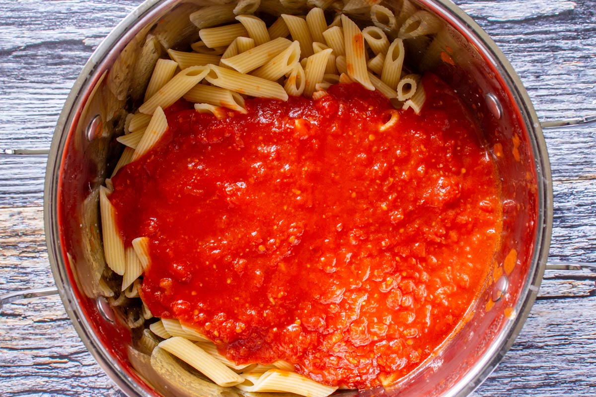 Penne pasta in a metal pot topped with arrabbiata tomato sauce.